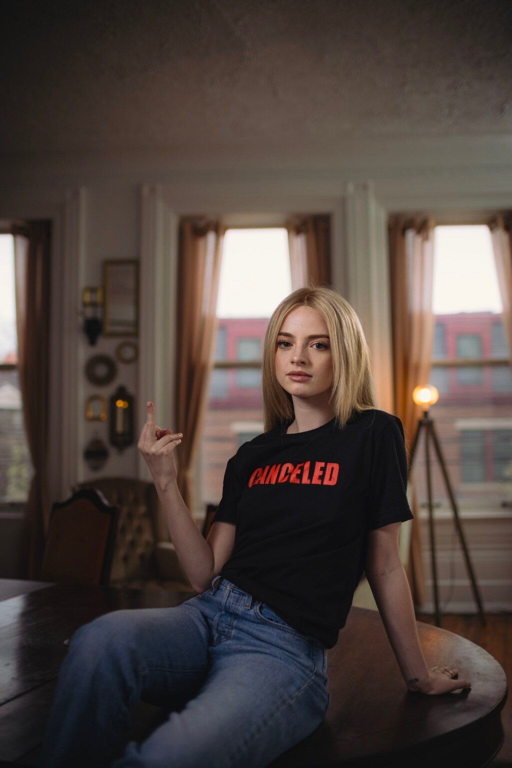 Madison Campbell seated on a table wearing a black CANCELED T-shirt and jeans